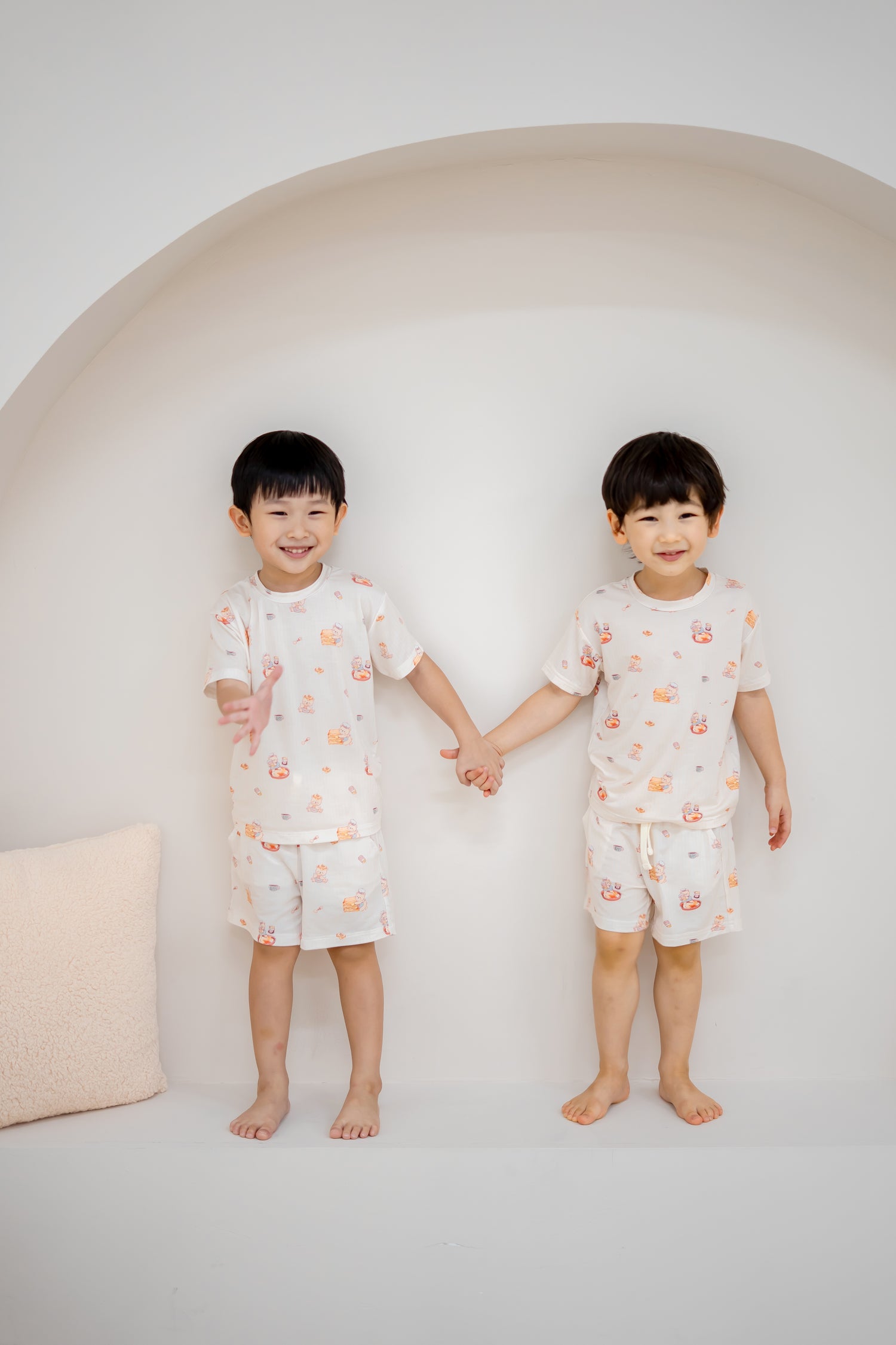 Two children holding hands in matching LeBear Kaya Butter Toast Kids TENCEL™ Lounge Sets with playful print.