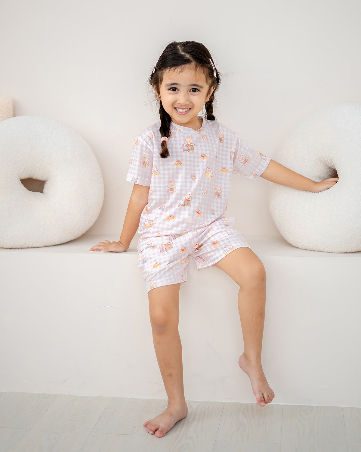 Girl sitting while wearing LeBear Bearista Blush Gingham kids bamboo lounge set with a cute café-inspired bear print.