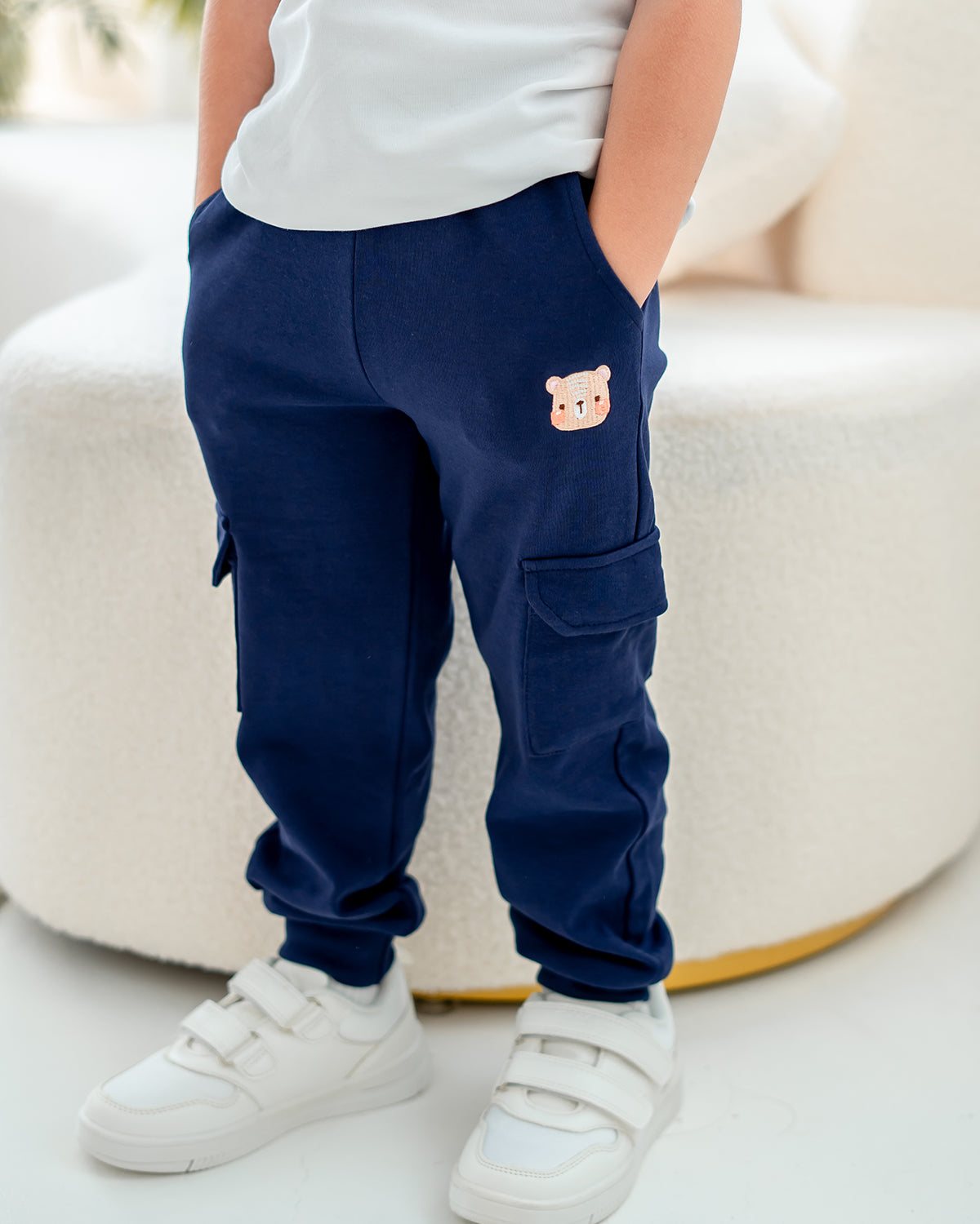 Boy in navy blue LeBear jogger pants with bear embroidery, hands in pockets