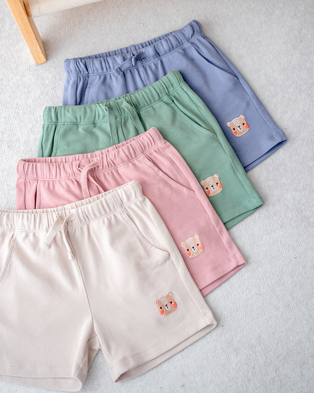 Set of four LeBear premium cotton jogger shorts for kids in lilac blue, sage green, blush pink, and cream beige, soft and breathable fabric.