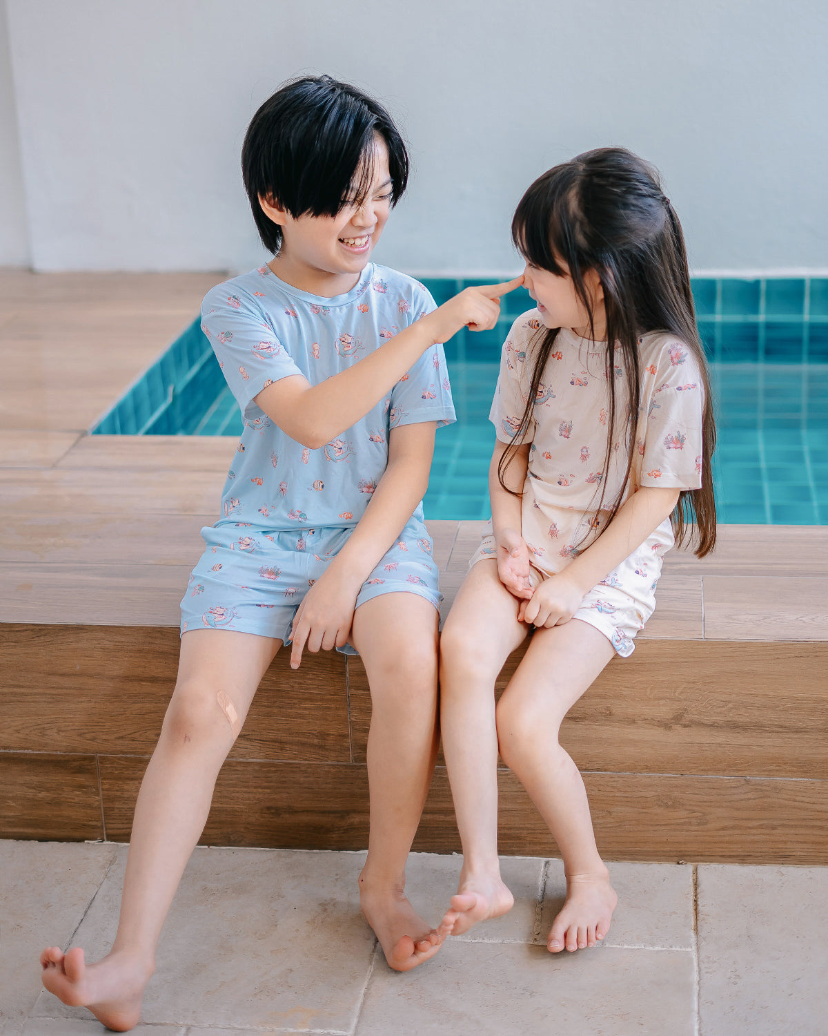 Siblings wearing LeBear Wander & Wonder Kids TENCEL lounge sets beside a pool.
