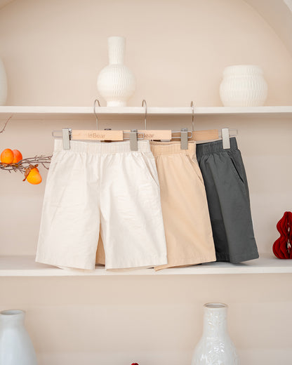 Three pairs of Everyday Essential Shorts hanging on a rack – kids neutral shorts in sand, cream and charcoal