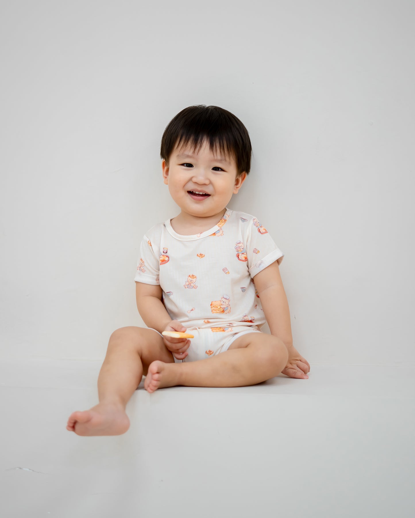 Baby sitting and smiling in LeBear Kaya Butter Toast TENCEL™ Baby Onesie with playful breakfast print.