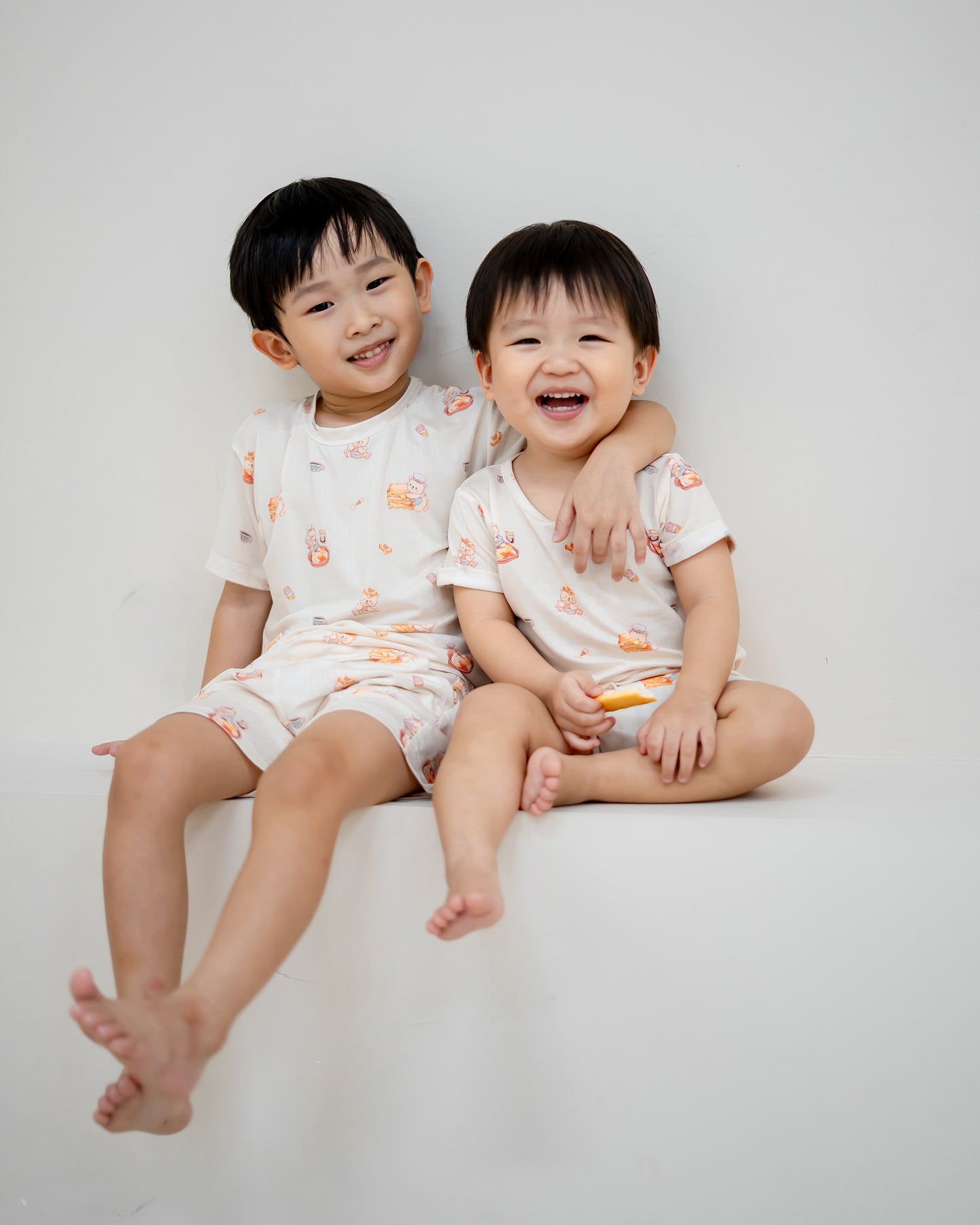 Two children smiling together wearing LeBear Kaya Butter Toast TENCEL™ sleepwear, featuring baby onesie and matching kids set.