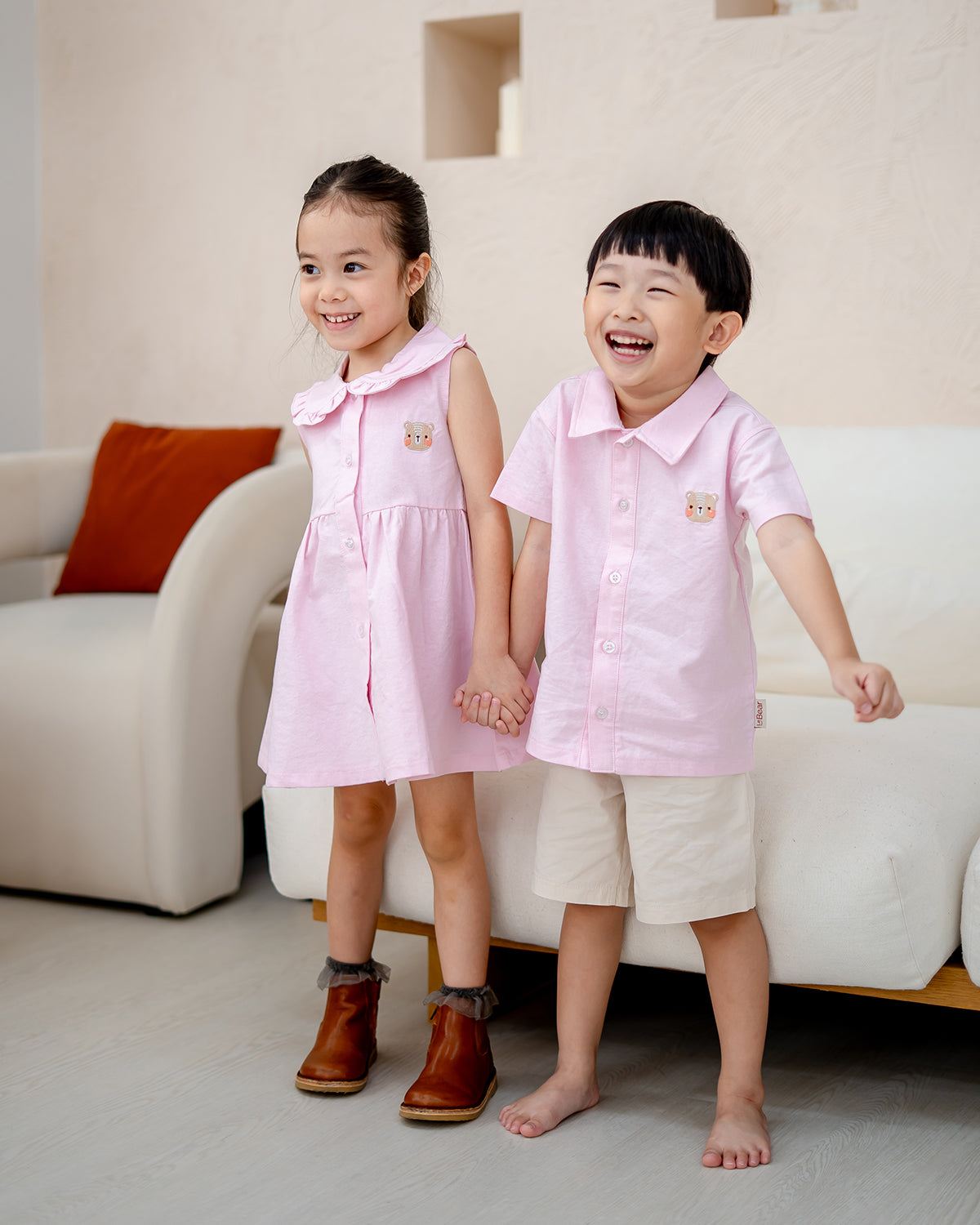 Little girl wearing LeBear Atelier Dress and boy in matching pink Atelier Shirt, holding hands and smiling