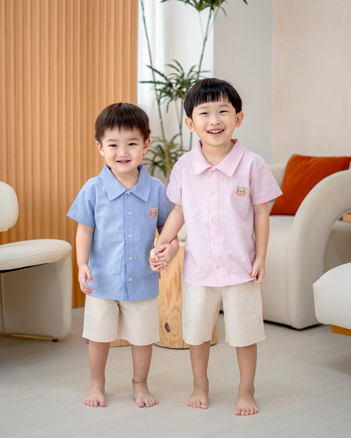 Siblings in LeBear Atelier Short Sleeve Button Down Shirts, blue and pink, holding hands indoors