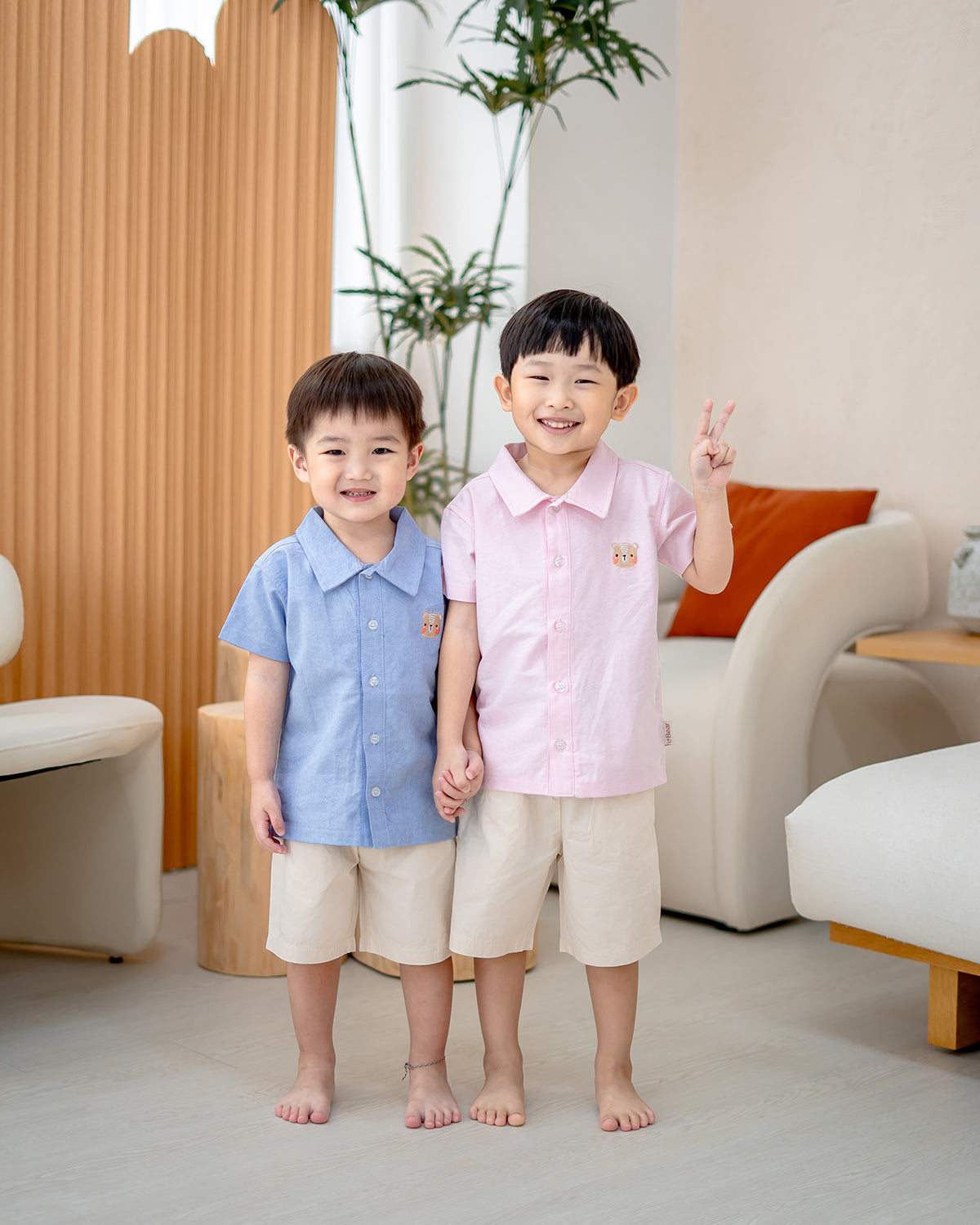 Two boys wearing LeBear Atelier Short Sleeve Button Down Shirts in pink and blue, styled with neutral shorts