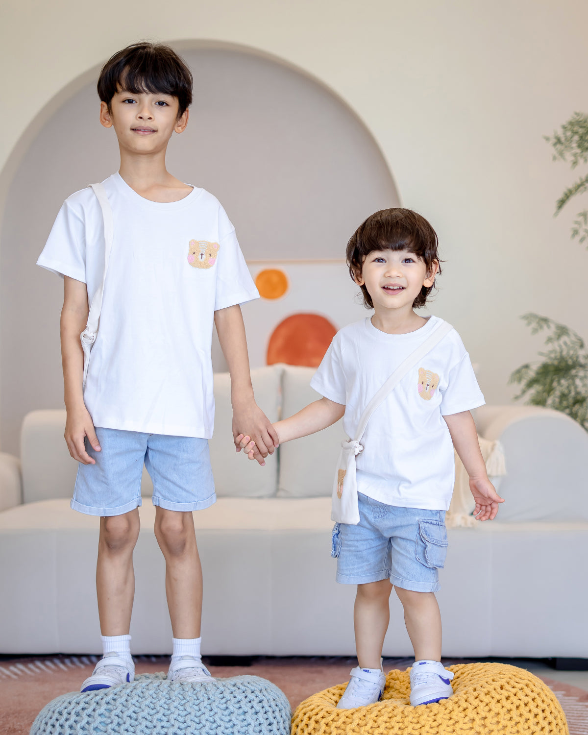 Two brothers wearing LeBear Fluffy Embroidery Kids Tee made from 100% premium cotton, smiling and holding hands in matching denim shorts – sibling outfit by LeBear Singapore.
