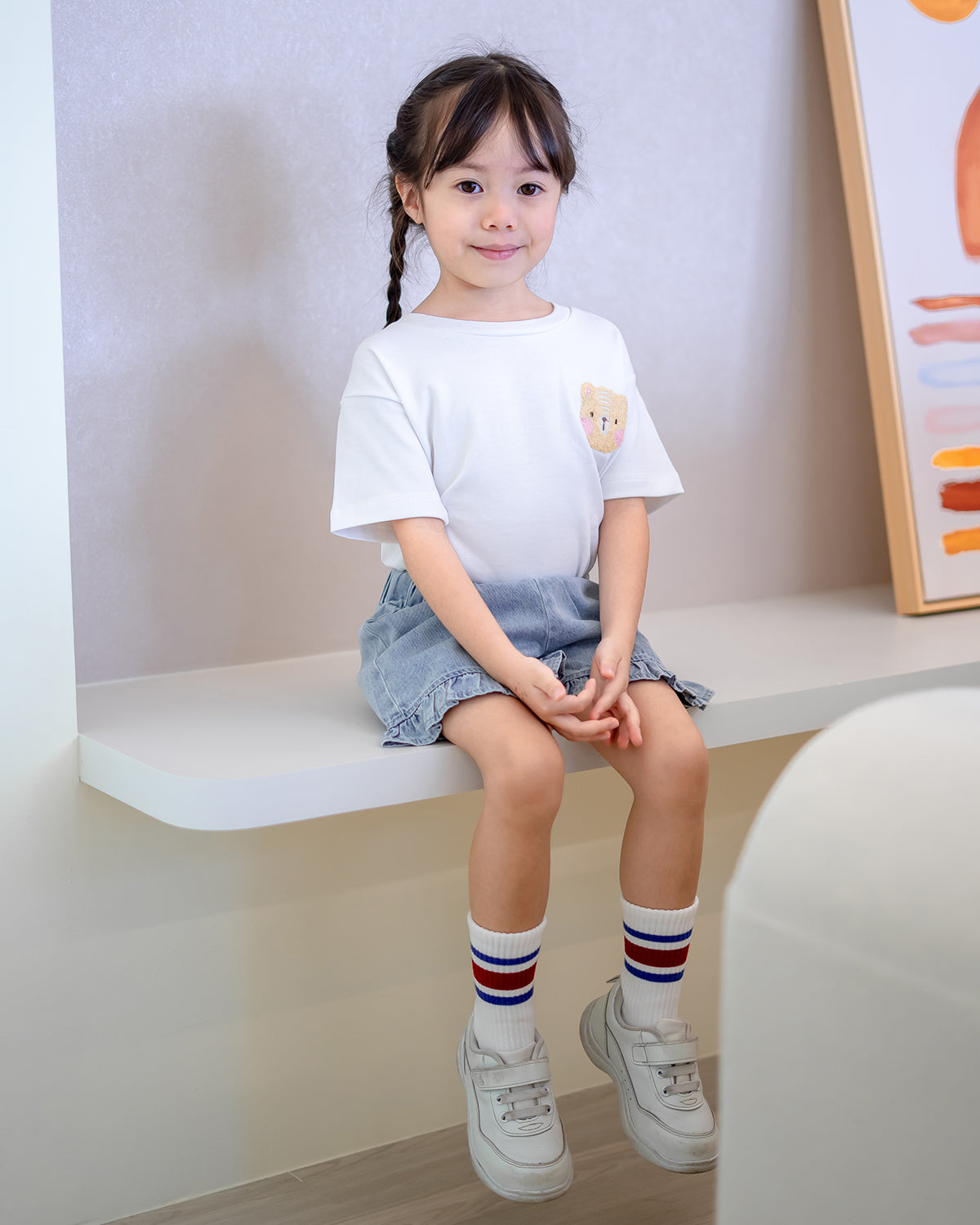 Girl sitting on a ledge in LeBear Fluffy Embroidery Kids Tee and denim shorts – soft premium cotton kidswear by LeBear Singapore.