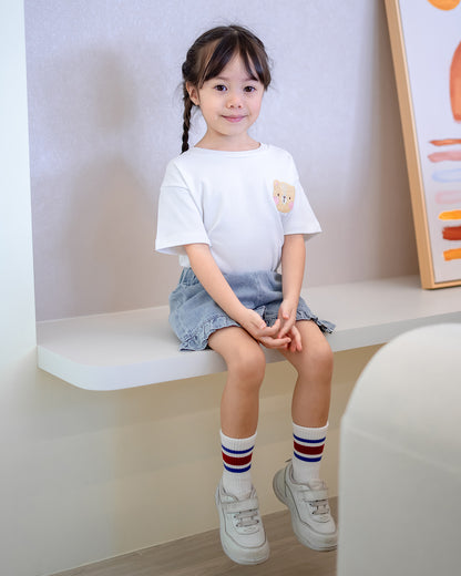 Girl sitting on a ledge in LeBear Fluffy Embroidery Kids Tee and denim shorts – soft premium cotton kidswear by LeBear Singapore.
