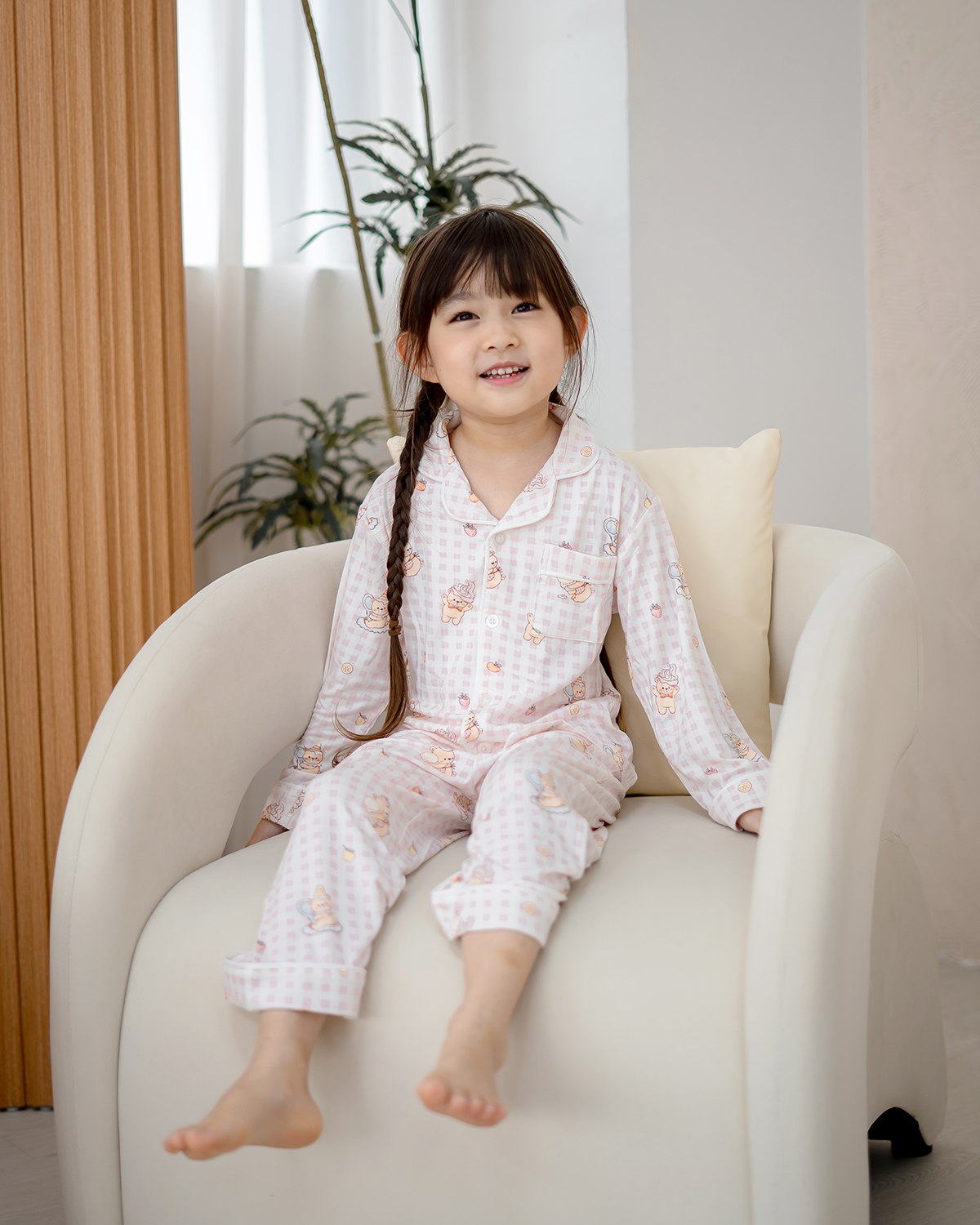Kid wearing LeBear Ice Cream Bear pink gingham bamboo pyjamas sitting comfortably on armchair