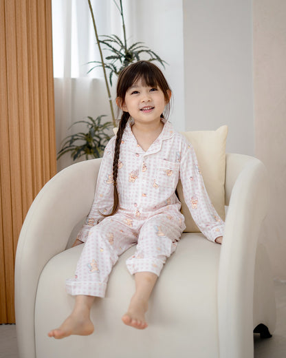 Kid wearing LeBear Ice Cream Bear pink gingham bamboo pyjamas sitting comfortably on armchair