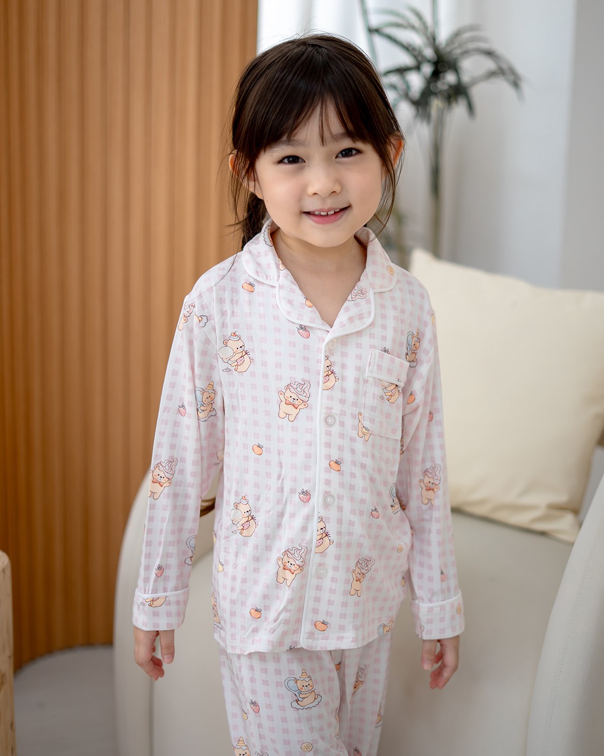 Child model wearing LeBear Ice Cream Bear pink gingham bamboo pyjamas standing and smiling in studio