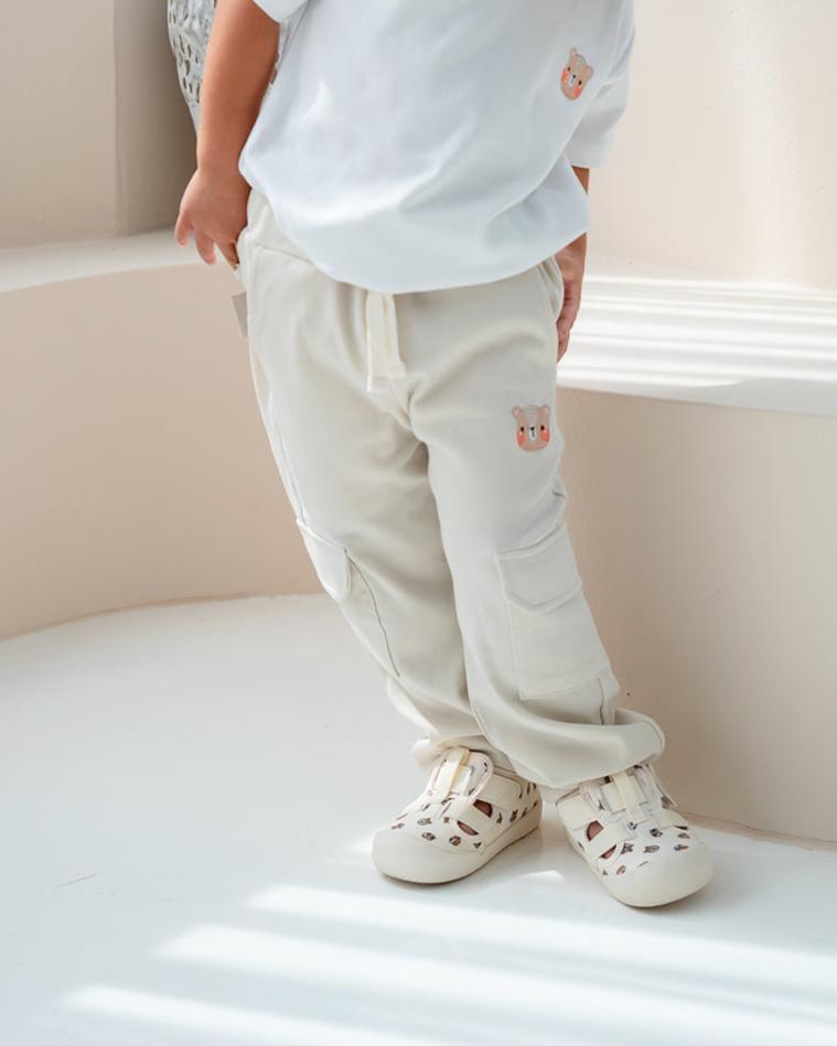 Child wearing cream LeBear jogger pants with bear embroidery, standing indoors