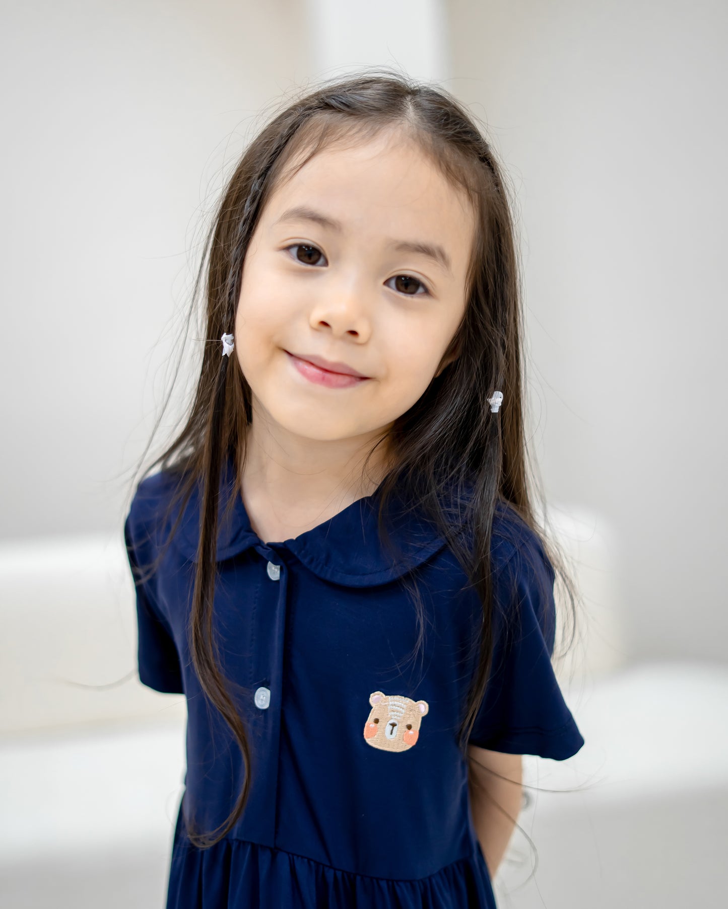Girl wearing LeBear Kids TENCEL™ Collar Dress in Navy with embroidered bear logo and rounded collar front close-up.