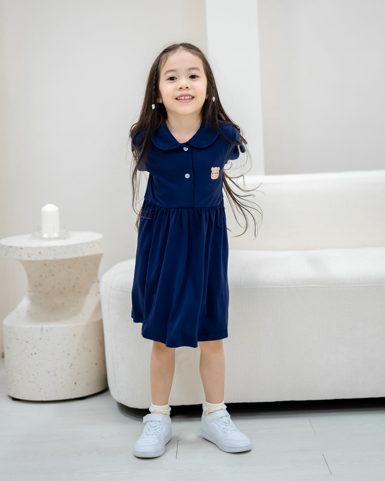 Child smiling in LeBear Kids TENCEL™ Collar Dress in Navy full body view with white sneakers.
