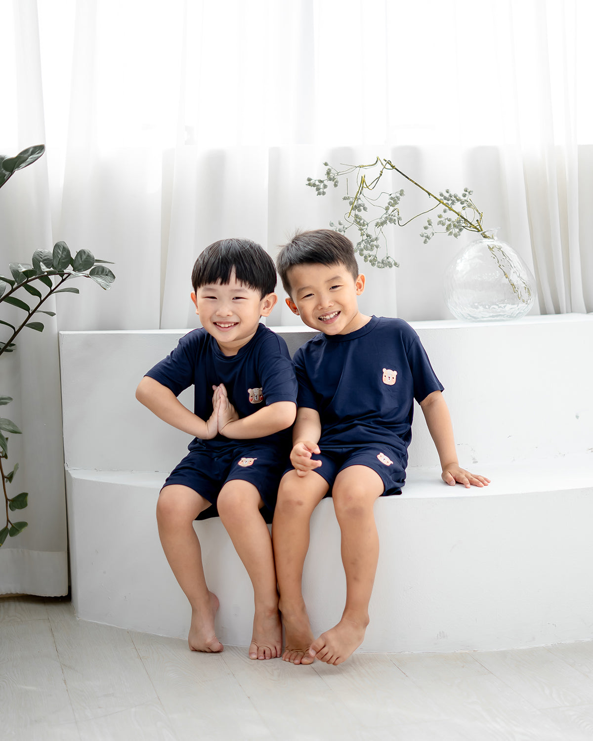 Two boys wearing LEBEAR Kids TENCEL™ Set in navy, smiling while seated on a white backdrop.