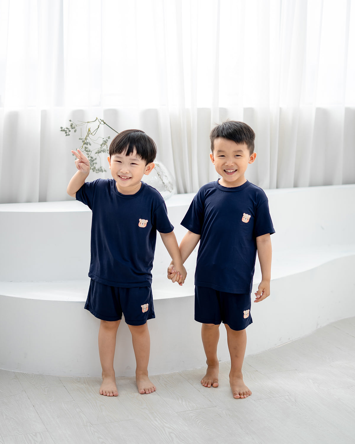 Kids wearing LEBEAR TENCEL™ Set in navy, standing hand in hand and smiling in soft natural light.
