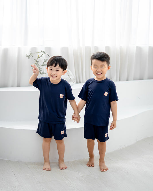 Kids wearing LEBEAR TENCEL™ Set in navy, standing hand in hand and smiling in soft natural light.
