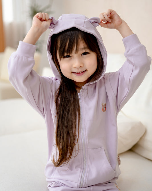 Child smiling while holding up bear ears on LeBear lilac hooded jacket, crafted from soft premium cotton.