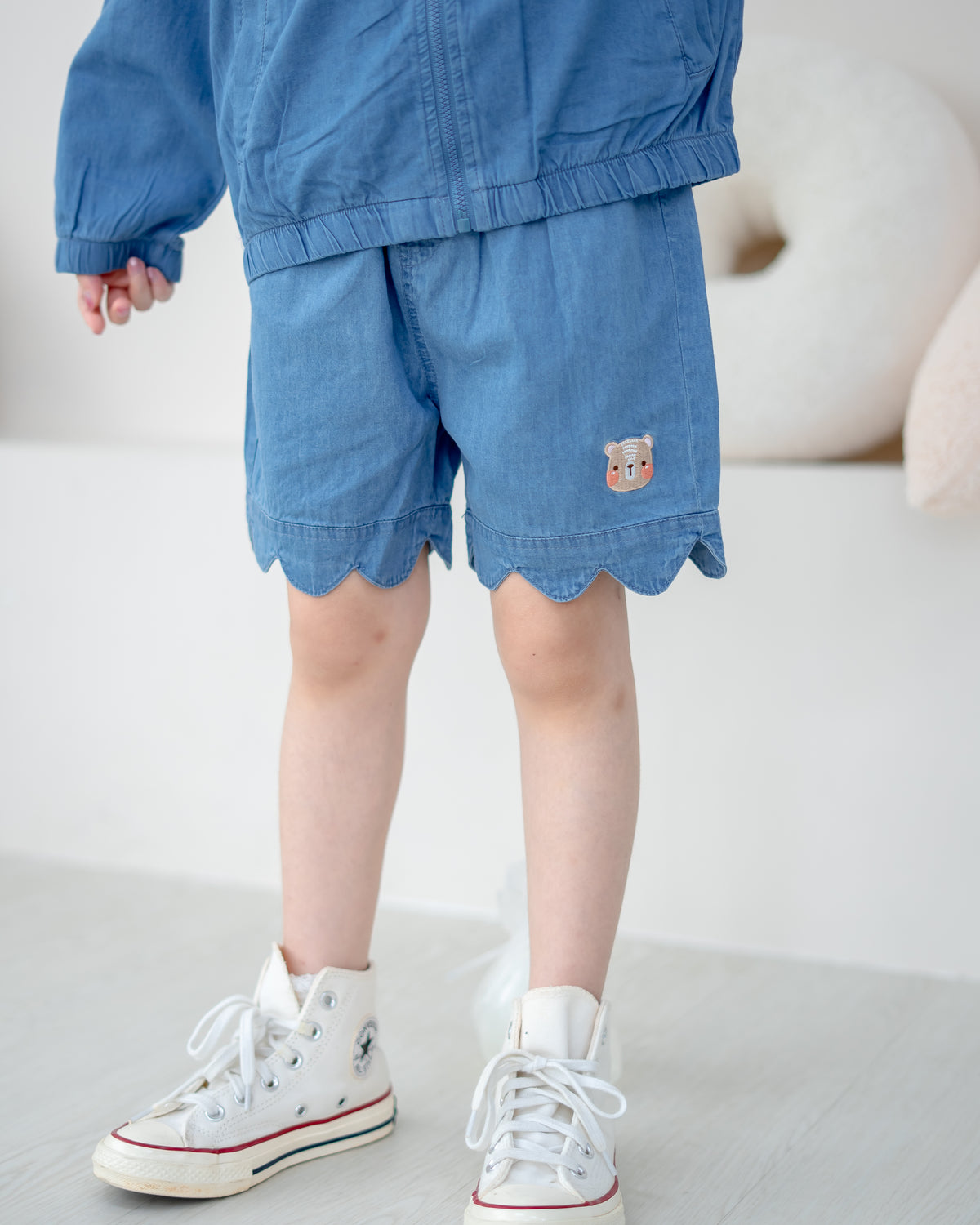 Close-up of LeBear kids denim shorts with scallop hem and bear embroidery