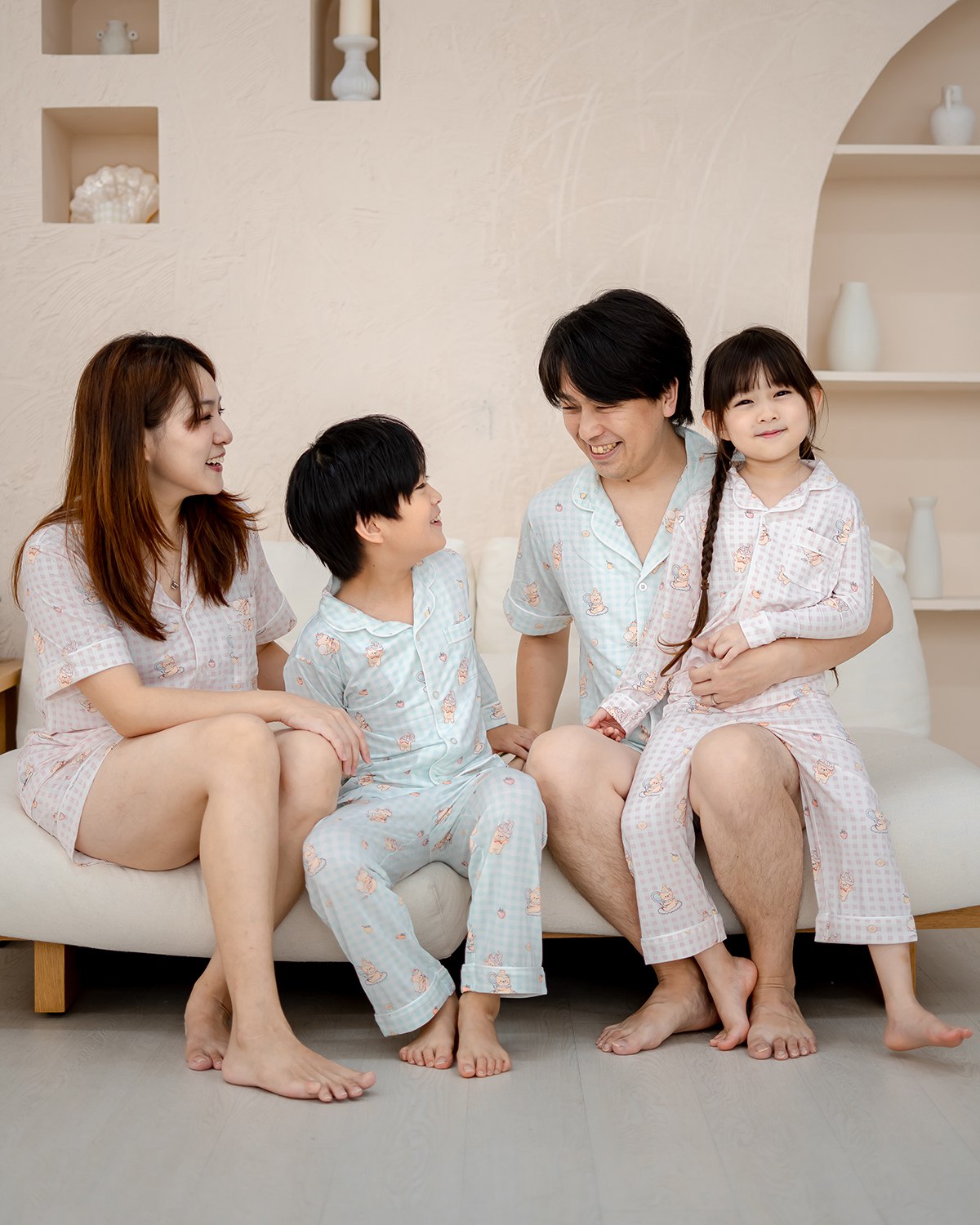 Family wearing LeBear Sweet Scoops Ice Cream Bear pink and blue gingham bamboo pyjamas sitting together on sofa