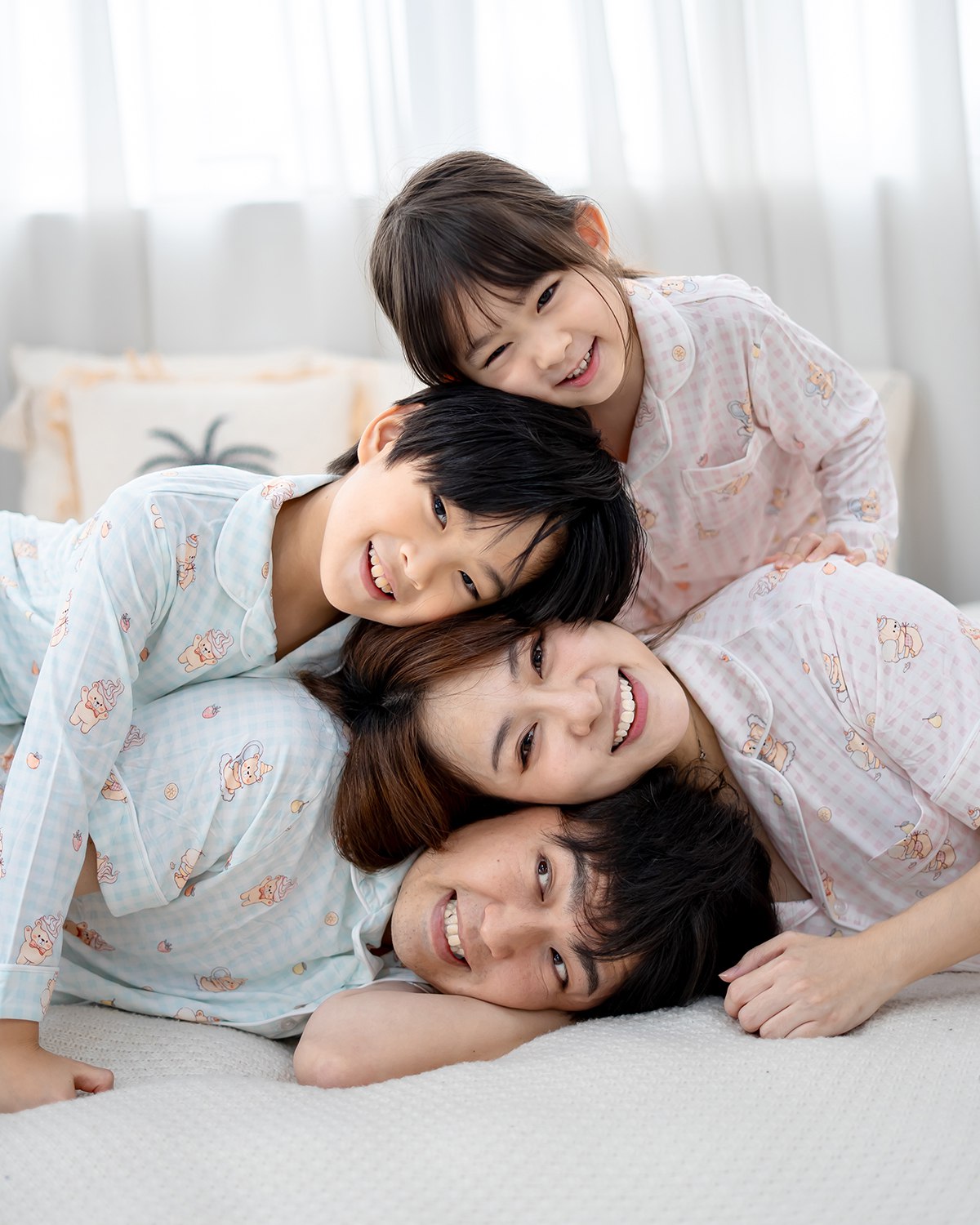 Family wearing LeBear Sweet Scoops Ice Cream Bear blue gingham bamboo pyjamas lying together and smiling