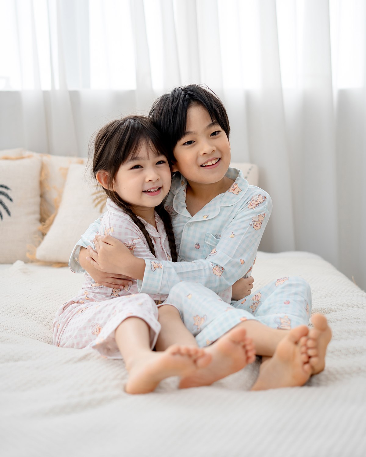 Brother and sister wearing LeBear Sweet Scoops Ice Cream Bear blue and pink gingham bamboo kids pyjamas hugging on bed