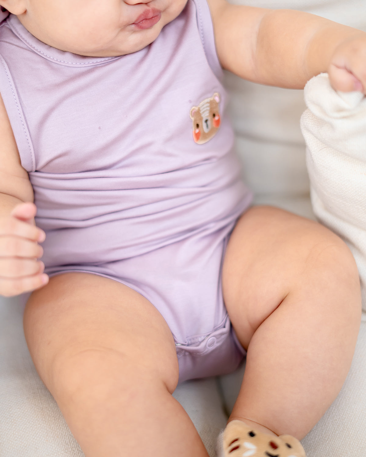 Close-up of LEBEAR TENCEL™ Onesie in Lilac showing signature embroidered bear logo.