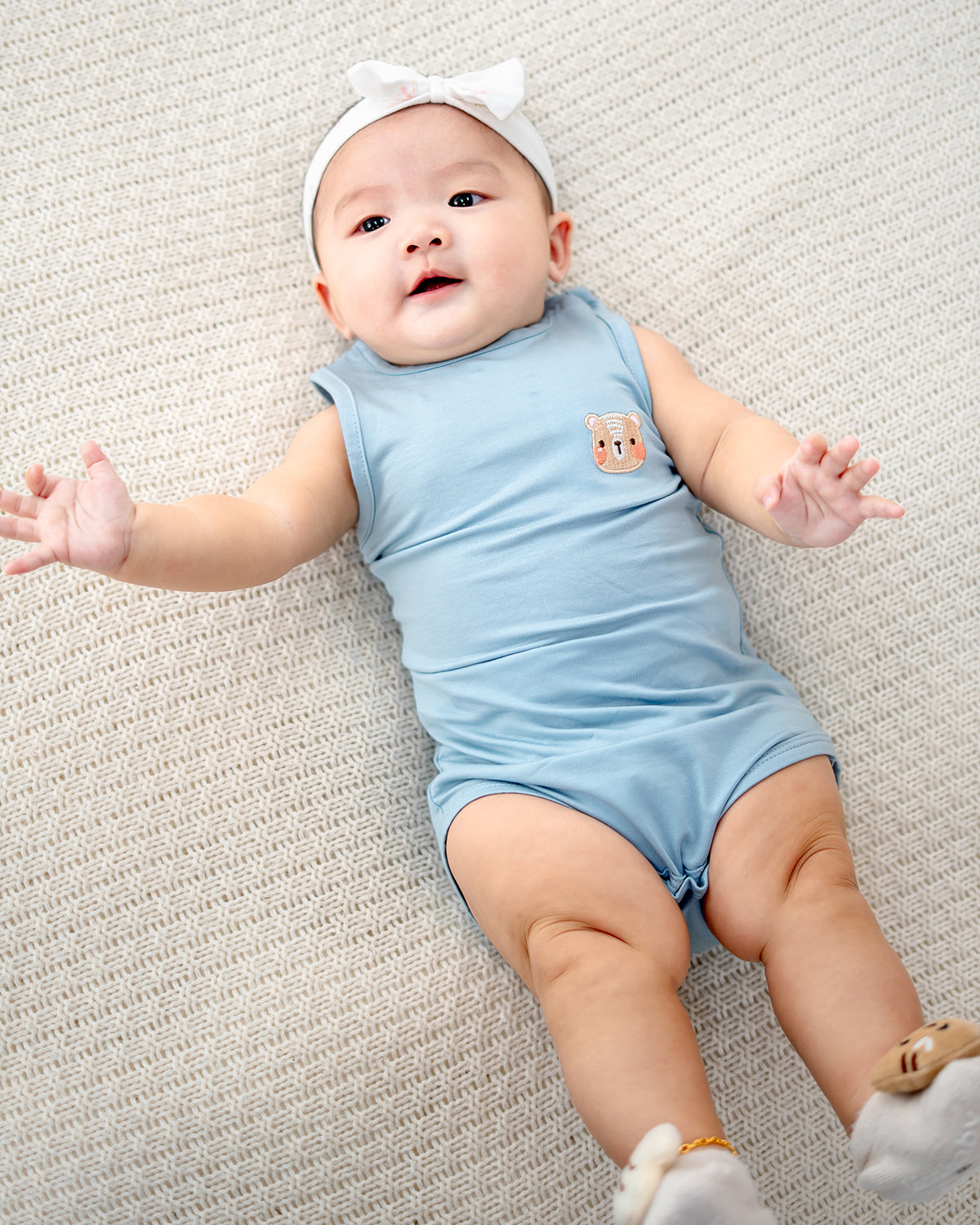 Close-up of TENCEL™ baby romper fabric and signature LEBEAR bear embroidery in sky blue.