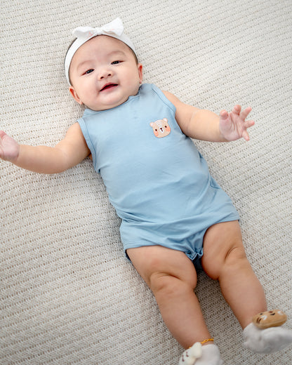 Baby girl smiling in LEBEAR TENCEL™ Sky Blue onesie with embroidered bear design.
