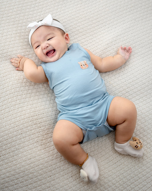 Baby wearing LEBEAR TENCEL™ Tank Onesie in Sky Blue lying on bed, soft breathable baby romper Singapore.