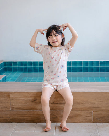 Girl wearing LeBear Wander & Wonder Kids Lenzing™ TENCEL™ Lounge Set in Seashell Sand beside a pool.